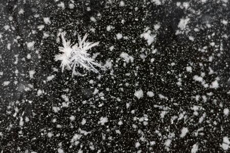 Real snowflake on a textured background of frost and ice crystals over black icy background.の写真素材