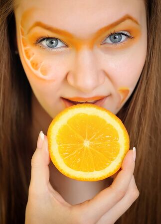 Young beautiful woman with creative orange makeup eating an orangeの写真素材