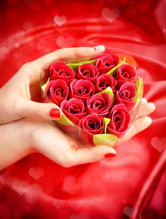 Heart-shaped box with red roses in women's hands against a background of red silkの写真素材