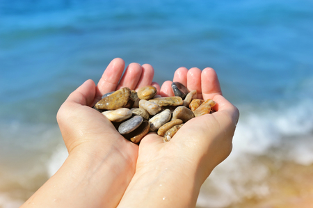 Handful of stones in hands, against seaの写真素材