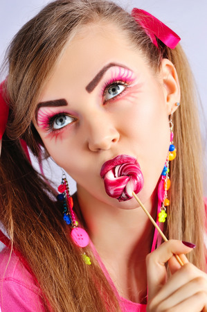 Beautiful woman with creative makeup licks colorful lollipopの写真素材