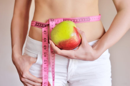 Young woman is measuring body and hold apple