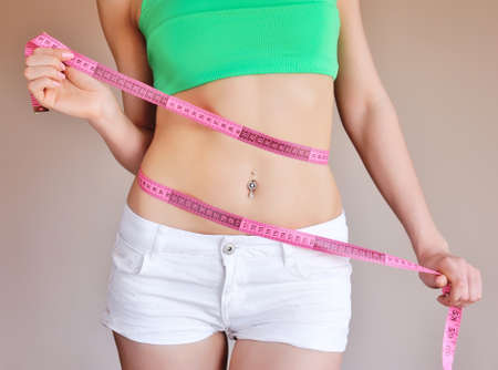 Close up of female hands measuring waist with measuring tape, dieting conceptの写真素材