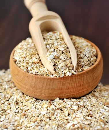 Oatmeal or oat flakes in bowl and scoop on dark wooden tableの写真素材
