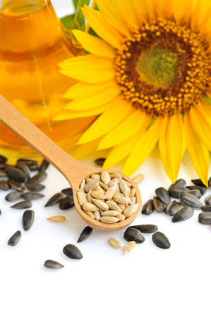 Wooden spoon with sunflower seeds on a background of flowers and a bottle of oilの写真素材