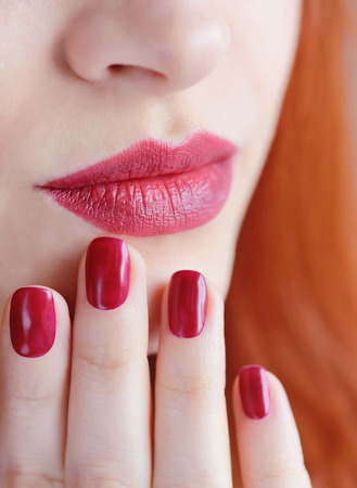 Beautiful red-haired young woman with red manicure, lipstick same color. Close up Portrait.の写真素材