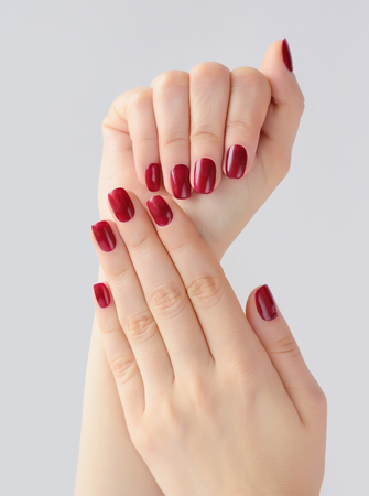 Closeup of hands of a young woman with red manicure on nails against white backgroundの写真素材