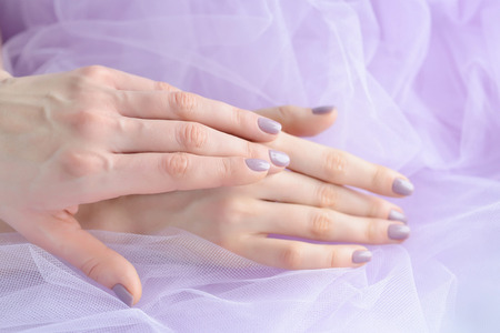 Closeup of hands of a young woman with pink manicure on nails against the background of a pink veilの写真素材