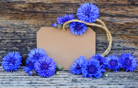 Paper tag with fresh cornflowers (Centaurea cyanus) on wooden tableの写真素材