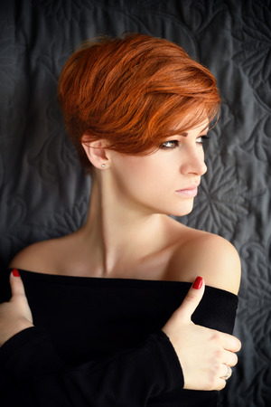 Portrait of a beautiful young red-haired woman with short hair on a dark backgroundの写真素材