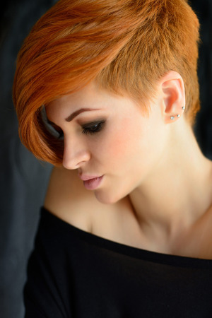 Portrait of a beautiful young red-haired woman with short hair on a dark backgroundの写真素材
