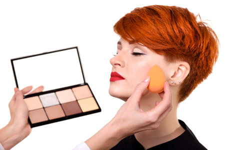 Makeup artist applying foundation on young woman's face using sponge. Beautiful young woman with...
