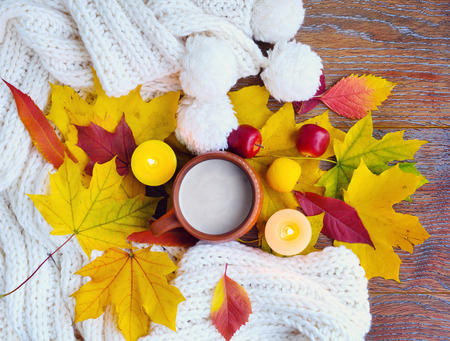 Autumn composition. Cup of coffee, colorful leaves, candles and scarf on wooden background. Top View.の写真素材
