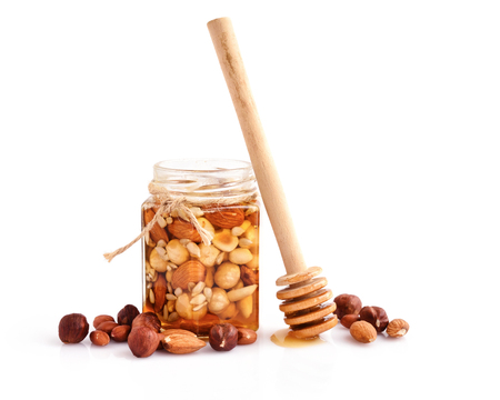 A honey jar with a spoon for honey and different nuts on white backgroundの写真素材