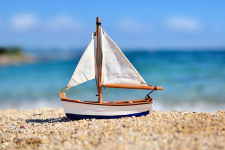 Miniature toy sailboat on the beach against the background of the sea and the blue sky. Vacation and...
