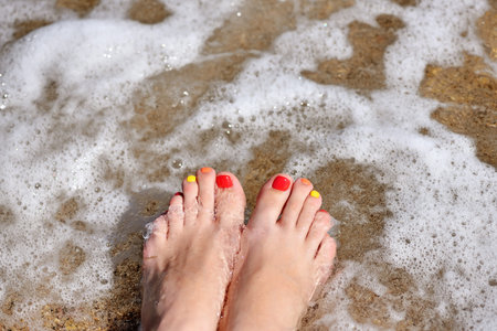 Wet women's feet on beach in sea surf. Vacation holidays