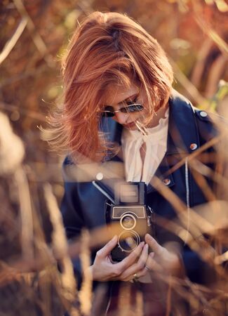 Beautiful young redhaired woman shoots on a retro cameraの写真素材