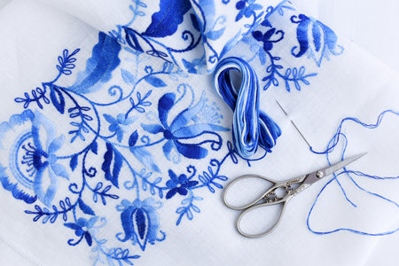 Embroidery, scissors, sewing needle and thread. Blue floral ornament on a white background. Top view