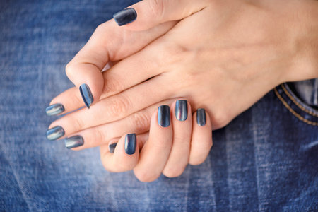 Hands with dark blue manicured nails on jeans textile backgroundの写真素材