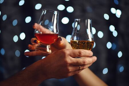 A couple makes a toast with two glasses of whiskey on festive backgroundの写真素材