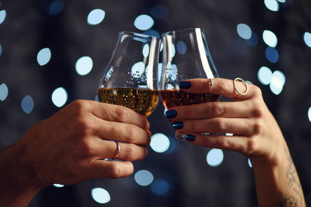 A couple makes a toast with two glasses of whiskey on festive backgroundの写真素材