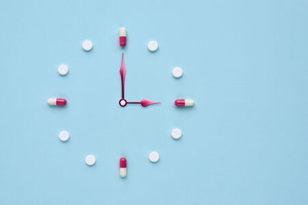 Clock created from pills and capsules on pastel blue background. Right time for using medicines. Flat lay.の写真素材