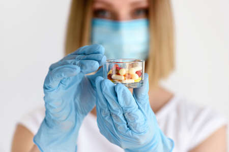 Woman's hands in gloves holds a glass with pills to be taken to her patient. Healthcare and medical concept.の写真素材