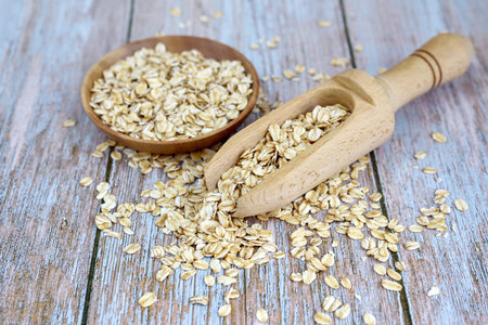 Oat flakes in the wooden scoop and bowl on rustic table. Healthy food for breakfast
