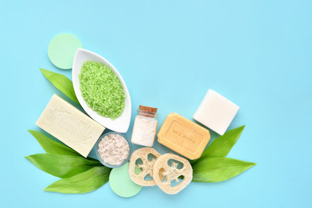 Organic spa cosmetic - bath salt, soap, sponge and green leaves on blue background. Healthy...