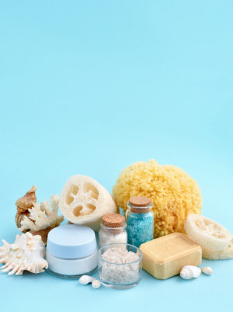 Spa accessories - sea salt, cream, sea sponge, soap and shells in cosmetics set for spa on blue...