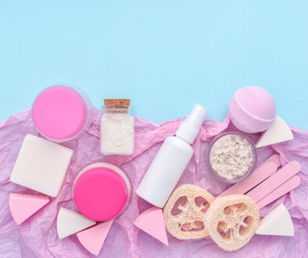 Skin care product - creams, lotion, soap, sponges, bath salt on pink and blue background. Flat lay...