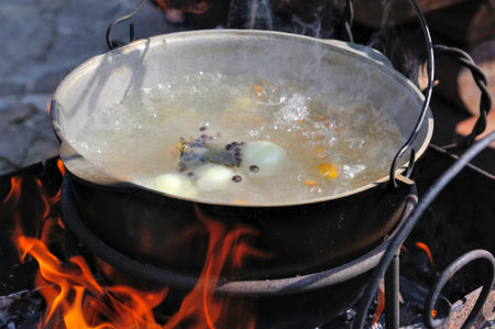 Cast-iron cauldron with soup at the stake in the courtyard. Cooking on an open fire. Soup with meat,...