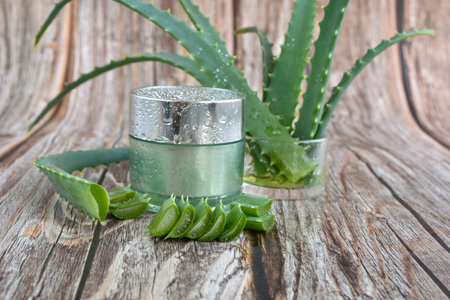 Fresh aloe vera leaves, cosmetic cream with aloe vera extract in glass container on wooden background. Natural cosmetics concept. For Health and beauty products.の写真素材