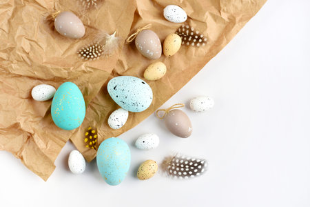 Easter eggs and feathers on a brown kraft paper background on a white table. Top view. For easter...