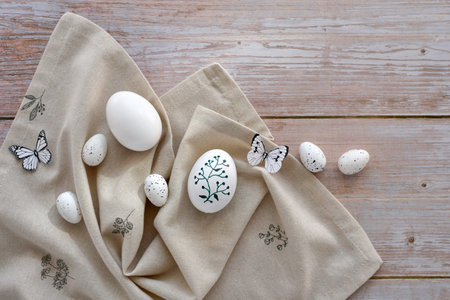 Stylish decorated easter eggs on linen cloth on a light wooden background. Top view. With space for...