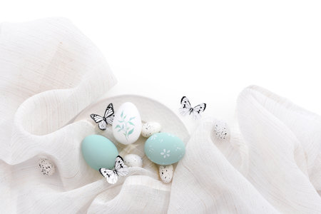 Stylish easter eggs and butterflys on linen cloth on white plate. Happy Easter concept. Top view. With space for your textの写真素材