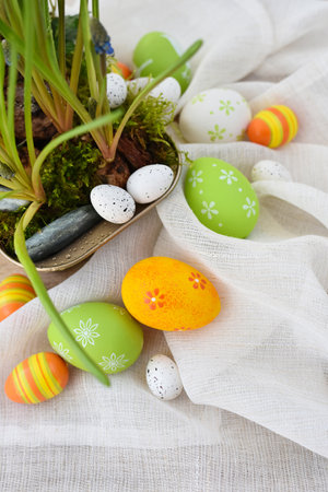 Colorful easter eggs on linen cloth and spring primroses in a pot. Easter still lifeの写真素材