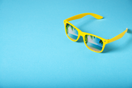 Yellow glasses isolated on blue background. Sea, palm trees are reflected in the glasses.の写真素材