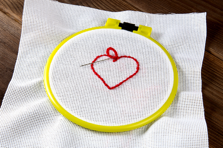 yellow hoop for embroidery with canvas and red threads on the table close-up, heartの写真素材