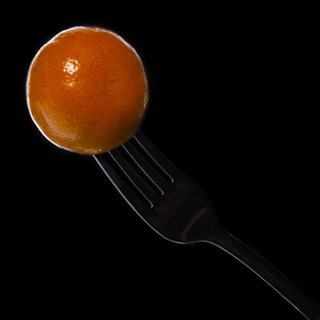 Mandarin pierced on a fork isolated on a black backgroundの写真素材