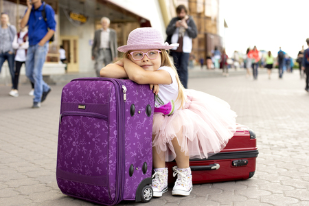 Little girl sitting on a suitcase at the railway station.の写真素材