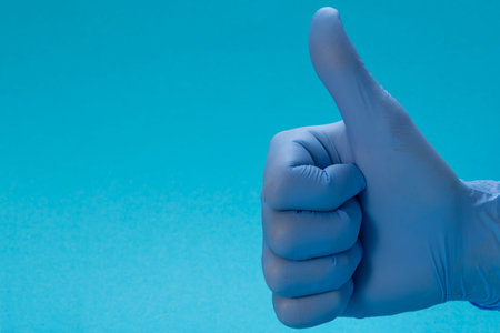 Hand in medical blue latex glove giving the thumbs up sign. Blue background. Great cleaning