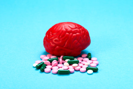 Red brain on a blue background with pink pills. Some pills for the brain. It is symbolic for drugs,...