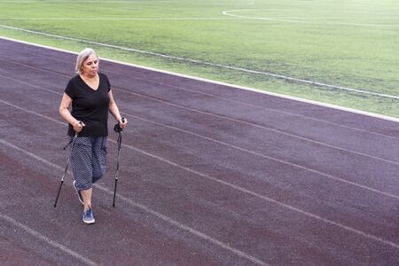 Elderly woman doing Nordic walking in a sports stadium.のeditorial素材