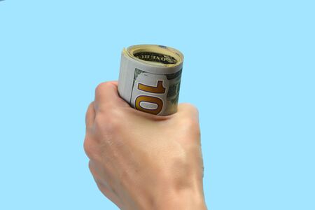 A hand is holding dollar bills rolled into a roll on a blue backgroundの写真素材
