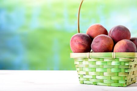Fresh peaches on a wooden table next to the basketの写真素材