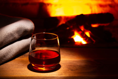 Glass of alcoholic drink wine in front of warm fireplace. Magical relaxed cozy atmosphere near fire.の写真素材