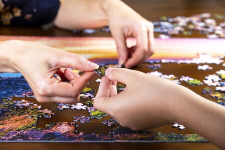 Minsk, Belarus, Aug. 11, 2019. Children and adult hands stack a color puzzle on a wooden tableのeditorial素材