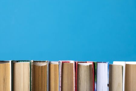 Simple composition of hardback books, raw books on wooden deck table and blue background. Stacking books without inscriptions, empty spine. Back to school. Open book. Place for text.の写真素材