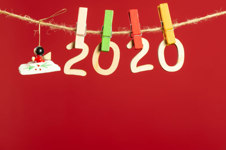 Christmas composition with wooden figures 2020. Figures hang on clothespins on a twine on a red...
